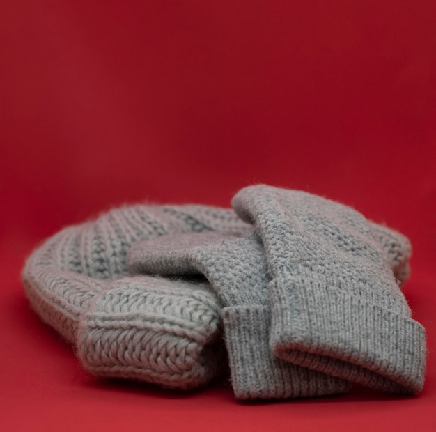 Gray wool mittens and hat on red background