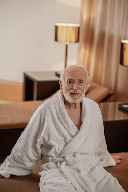 A grayhaired bearded man in a white robe in a hotel room