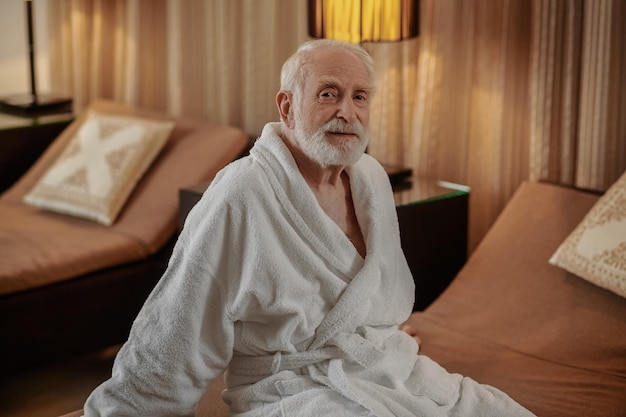 A grayhaired bearded man in a white robe in a hotel room