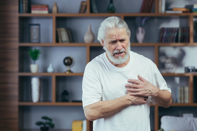 Photo grayhaired man has severe chest pain grandfather's heart aches holds hands on his chest at home