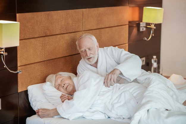 A grayhaired man looking with tenderness at his wife while she sleeping