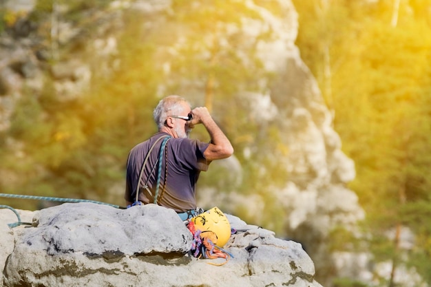 The grayhaired man sitting on a rock on a background of forest and mountains