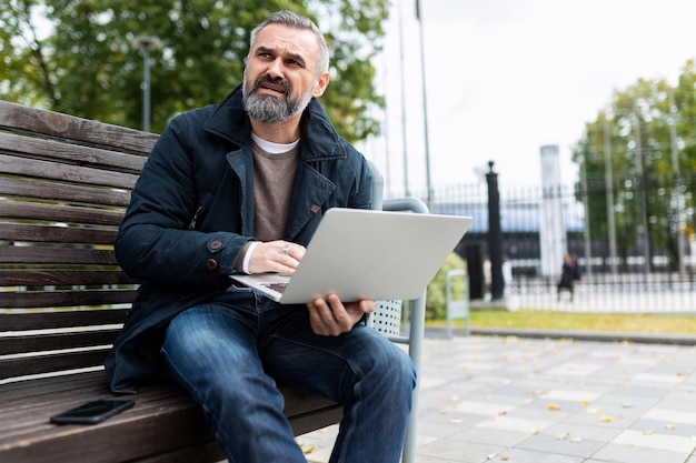 Седой зрелый мужчина с ноутбуком на улице