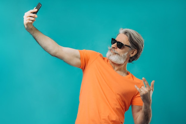 Седой пожилой мужчина в солнцезащитных очках позирует с телефоном Студийная съемка