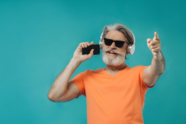 Grayhaired senior man in sunglasses posing with a phone Studio shooting