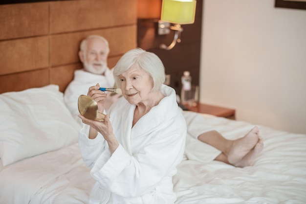 A grayhaired woman doing make up in the morning