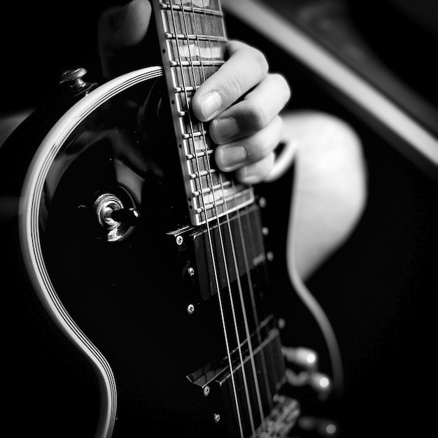 Grayscale closeup shot of an electric guitar and a person's hand holding its fretboard