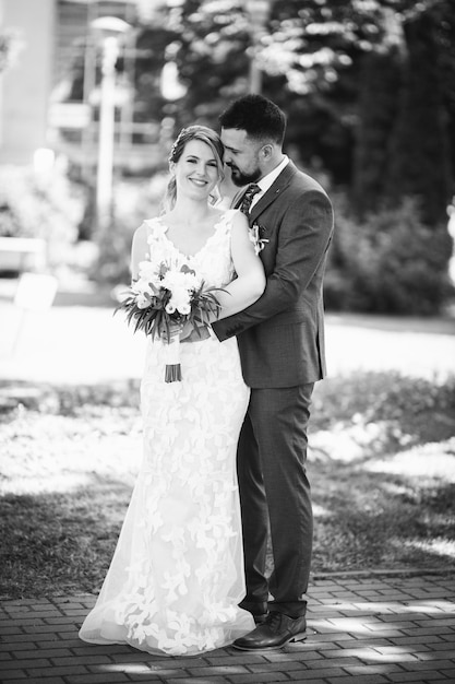 Grayscale fullbody portrait of a cheerful wedding couple posing in the park
