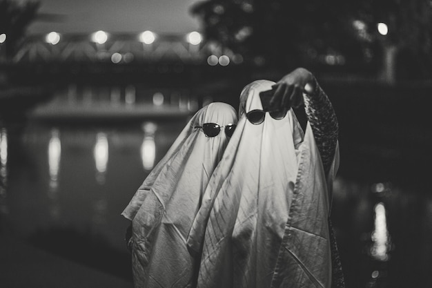 Photo grayscale funny image of two people in ghost costumes and sunglasses taking a selfie