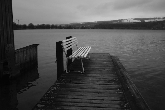 Grayscale of a lonely bench on a pier at the sea