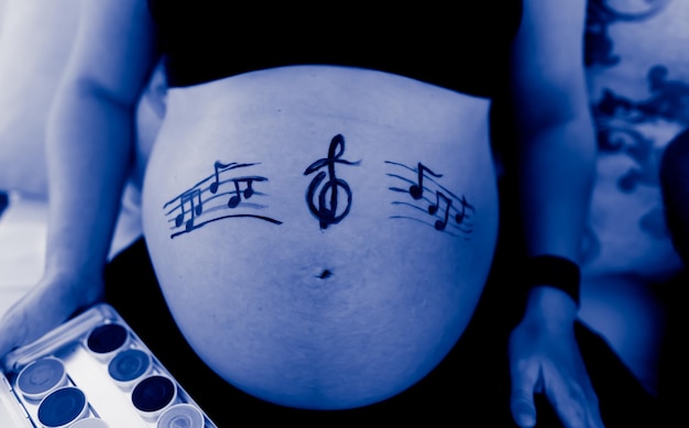 Photo grayscale selective focus shot of music notes on pregnant belly