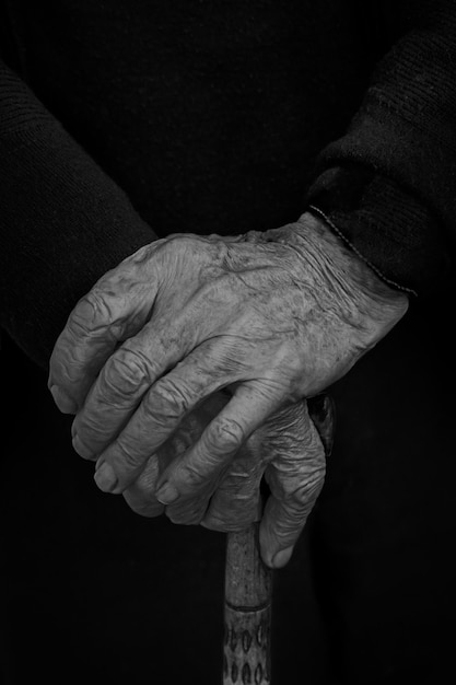 A grayscale shot of old man hands on his wooden walking stick