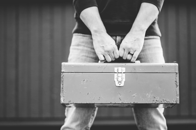 Grayscale shot of a technician holding a toolbox outdoors with a blurry background