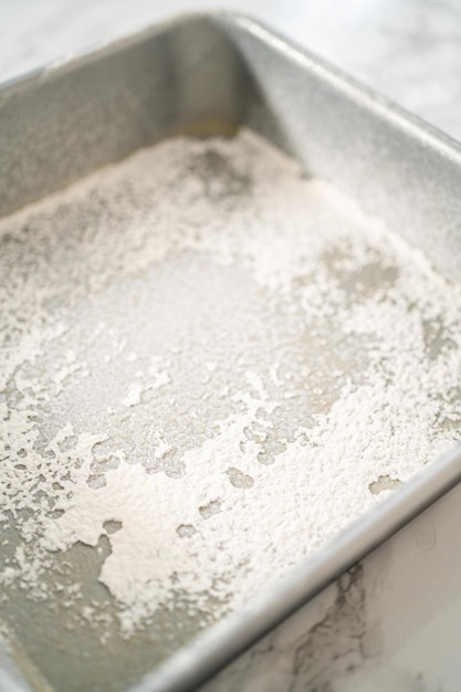 Greasing metal square baking pan to bake sweets.