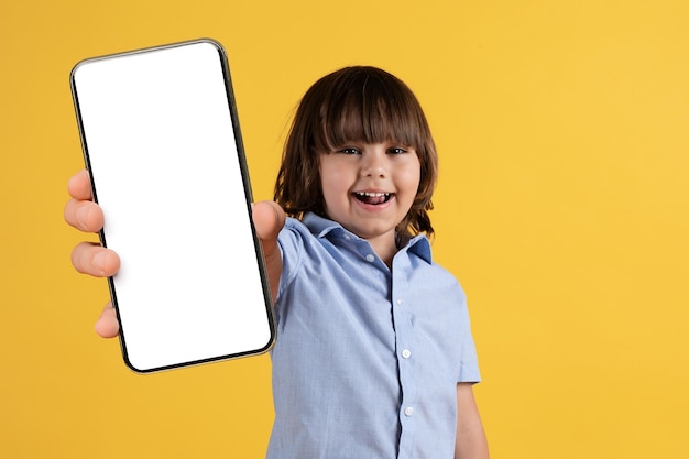 Great app for kids happy little boy showing smartphone with blank screen to camera orange background empty space