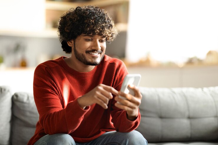 Photo great app smiling indian man using modern smartphone at home