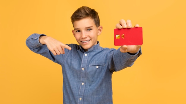 Great bank happy teen boy pointing at credit card in hand