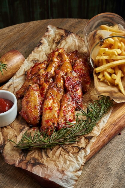 Great beer snack - spicy baked buffalo wings. BBQ wings with garnish of french fries on a wooden tray. Top view, food flat lay. Pub food