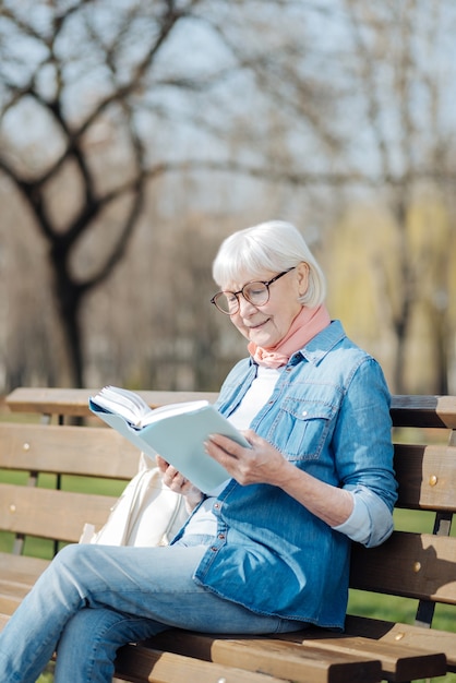 Ottimo libro. donna bionda allegra che legge un libro mentre era seduto sulla panchina