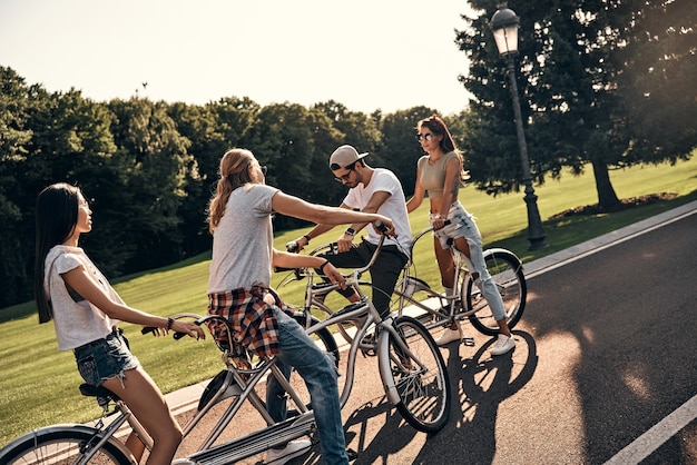 Great day for a bike ride. Group of young modern people in casual wear cycling while spending carefree time outdoors