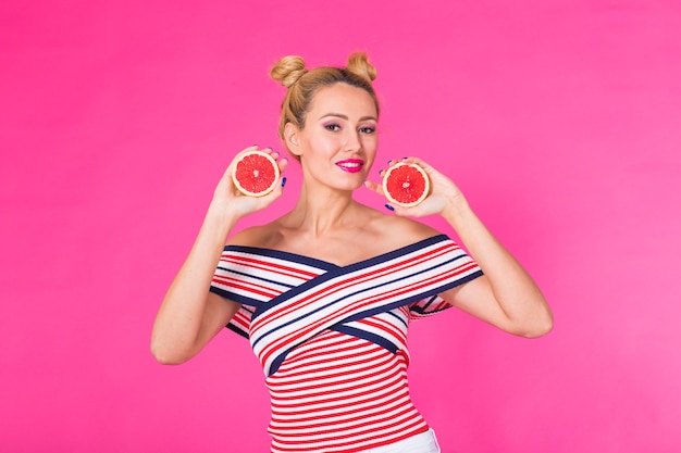 Great food for a healthy lifestyle. Beautiful young woman holding piece of orange against pink