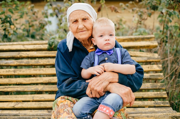 great grandmother holding great grandson on her knees outdoor.