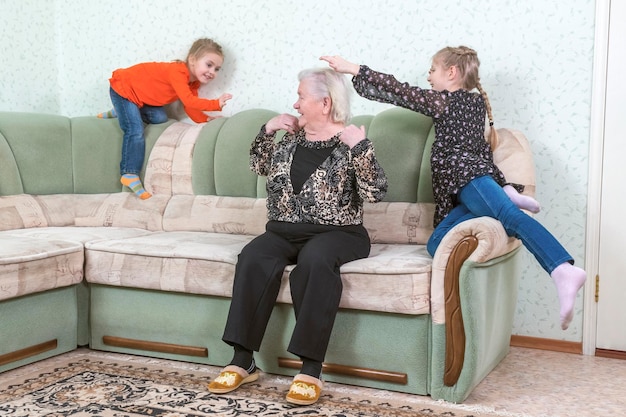 Great-grandmother plays with her granddaughters in catch-up on the sofa in the hall