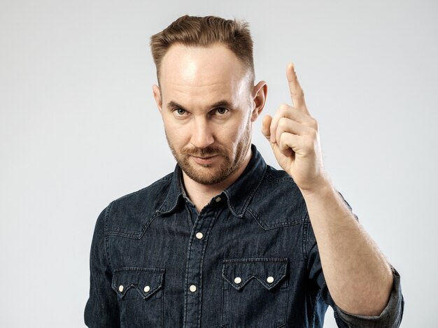 Great idea! Portrait of confident young man touching finger up isolated on gray background