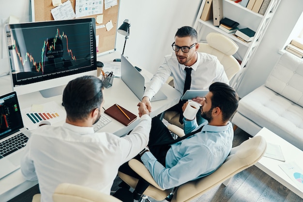 Great job! Top view of young modern men in formalwear shaking hands while working in the office