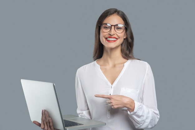 Ottimo laptop. giovane donna d'affari di gioia con lunghi capelli scuri che indossano occhiali tenendo la mostra portatile