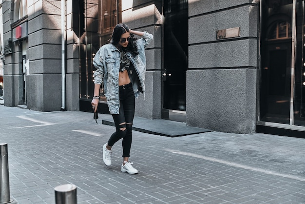 Photo great look. full length of beautiful young woman in jeans jacket keeping hand in hair