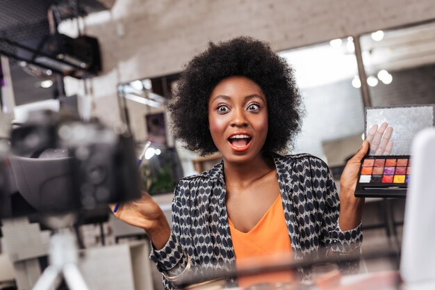 Great mood. Beautiful dark-skinned woman with curly hair looking excited while conducting a fashion online tutorial