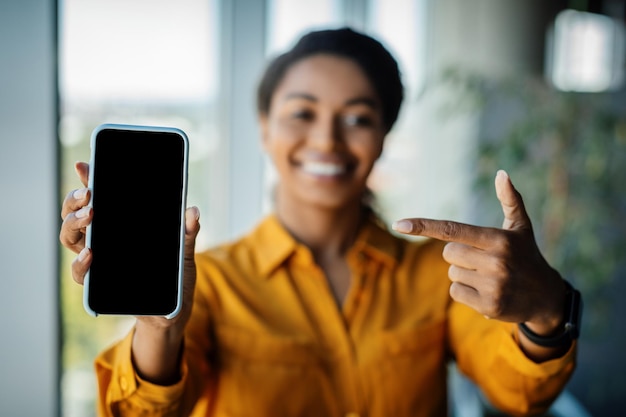 Great offer Black businesswoman holding and pointing finger at cellphone with empty screen promoting app or website