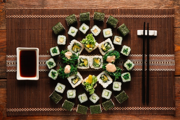 Great ornament of vegetarian sushi rolls set served on brown straw mat, flat lay. Japanese traditional cuisine, food art, culinary masterpiece.