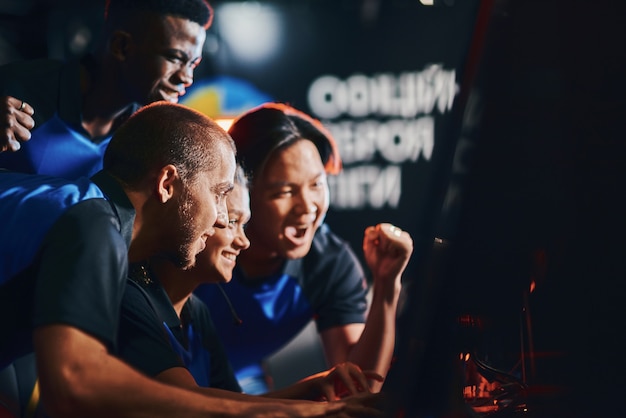 Great result. Team of excited professional cybersport gamers looking at PC screen and celebrating success while participating in eSport tournament. Playing online video games