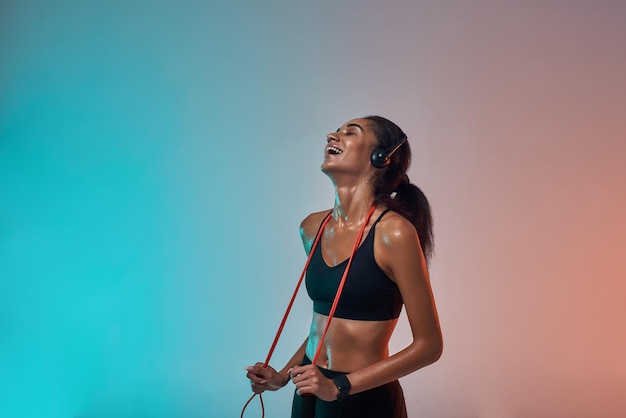 Great workout side view of happy young woman in headphones holding jumping rope on shoulders