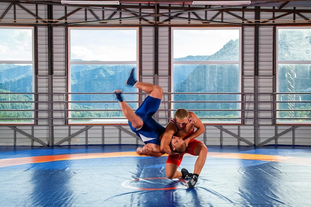 赤と青のユニフォームを着た2人のギリシャ・ローマのレスラーと格闘するギリシャ-ローマのレスリングのトレーニング