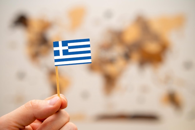 Greece flag in mans hand on the wooden world map background global economy and geopolitics concept