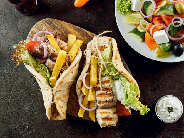 Foto giroscopi greci di fast food sullo sfondo scuro pollo alla griglia carne fritta patate foglie di insalata di lattuga verde