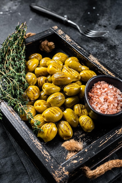 Greek Grilled olives with garlic olive oil and spices in wooden tray Black background Top view