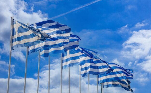 Греческий национальный официальный флаг на флагштоке, размахивающий в ряду Греческий знак символ облачное голубое небо