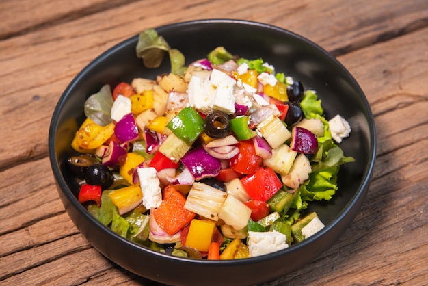 Greek salad in a black ceramic bowl, wooden table top