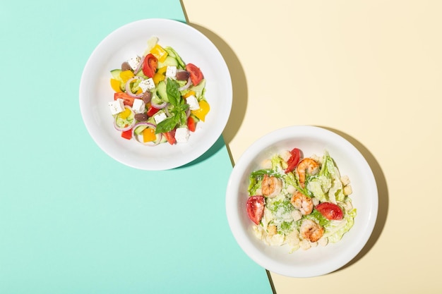 Greek salad and cesar salad in white plates hard shadows on blue and yellow high quality photo