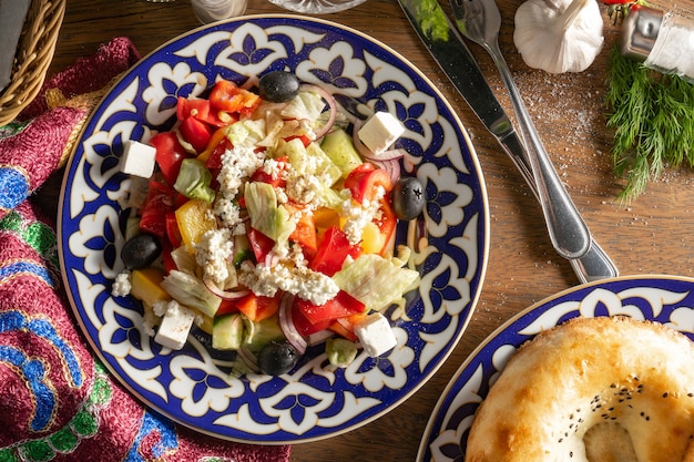 Greek Salad. Classic vegetarian vegetable salad with sweet pepper, cucumber, onion, olives and Feta cheese, dressed with olive oil in a plate with a traditional Uzbek pattern.