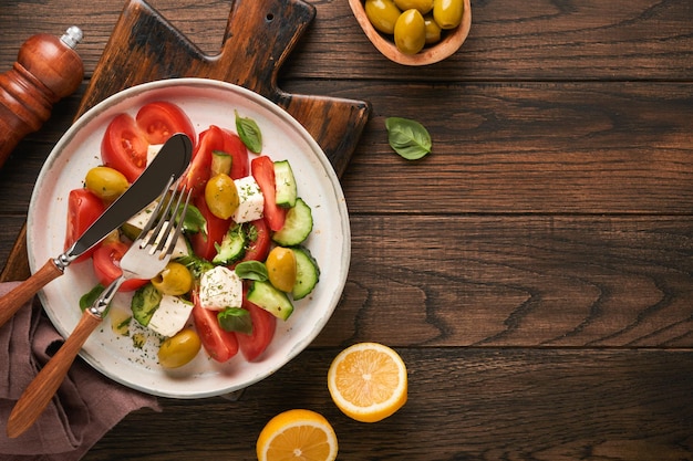 Greek salad Fresh Greek salad with fresh vegetables tomato cucumber green olives and feta cheese on old dark wooden table background Top view