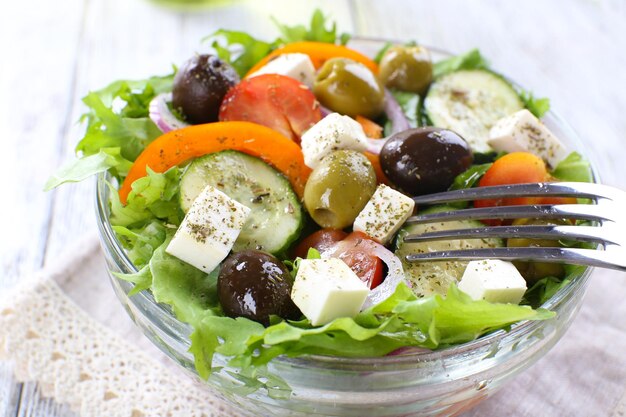 Greek salad in glass dish on napkin and color wooden background