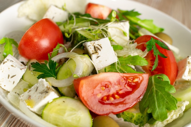 Greek salad or horiatiki with large pieces of tomatoes, cucumbers, feta cheese and micro greens sprouts closeup. Village salad with diced mozzarella, arugula, spices and olive oil