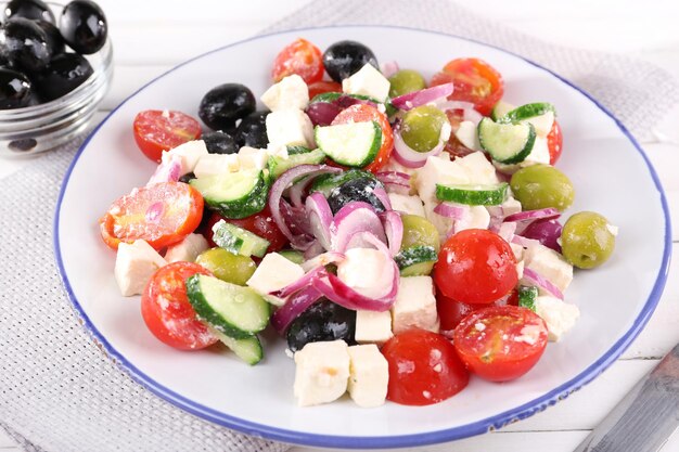 Greek salad served in plate on napkin on wooden background