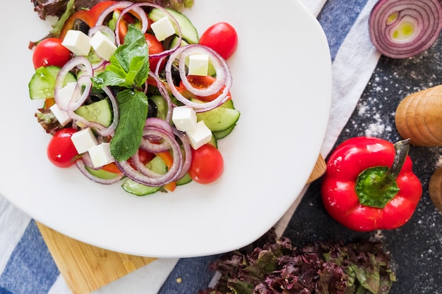 Greek salad on a white plate on dark stone background. Fresh food flat lay.