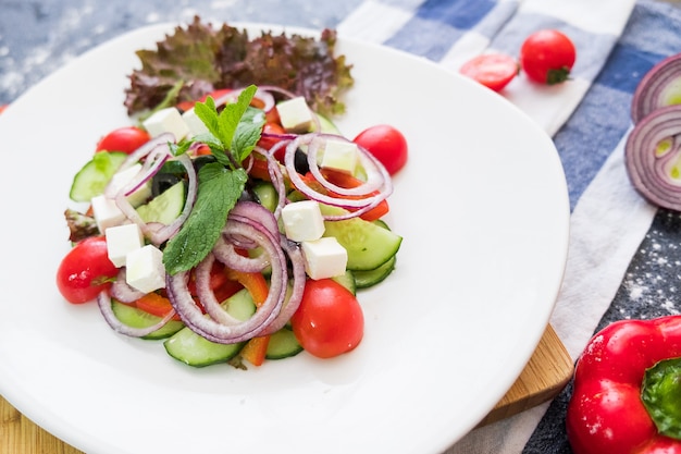 Greek salad on a white plate on dark stone background. Fresh food flat lay.